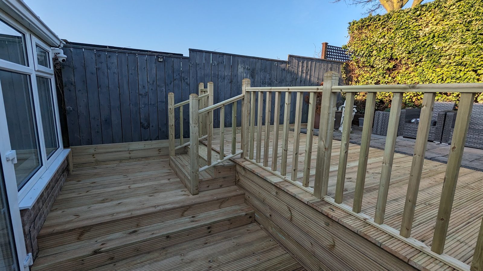 A raised timber deck with steps and a spindle balustrade beside a conservatory