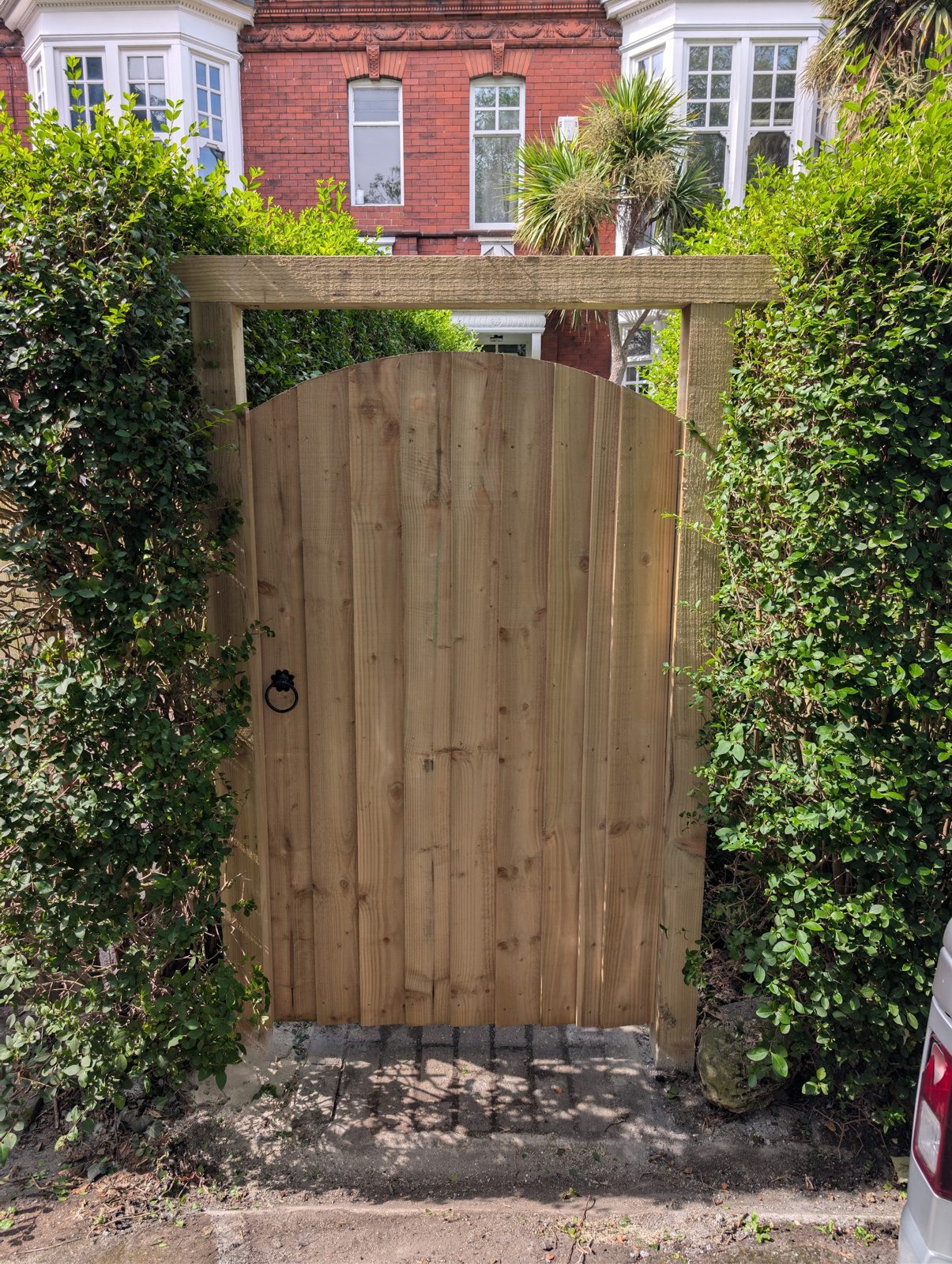 A made to measure arched timber gate in a timber frame between two hedges