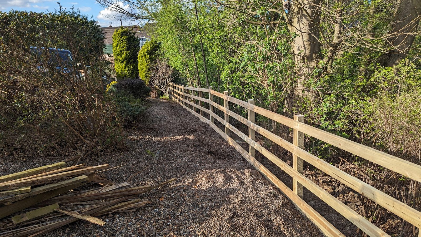 A new post and rail fence along a gravel path between trees